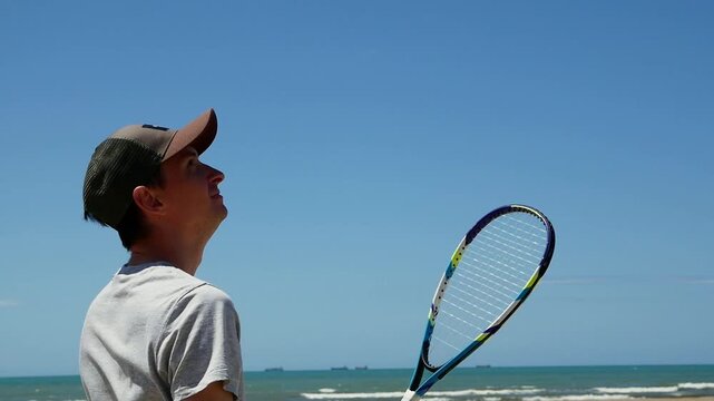 Man performing speed badminton serve on sandy beach, athletic training, shuttlecock practice, active lifestyle, summer outdoor fitness.