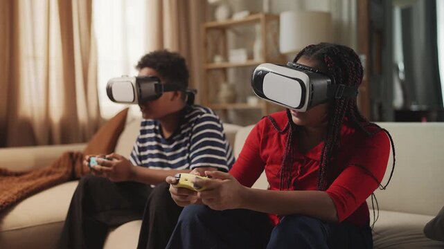 African American girl and boy in VR headsets playing video game with joysticks