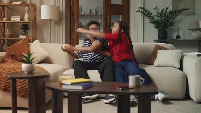 Smiling sister trying to take gamepad from her brother, playful home fun