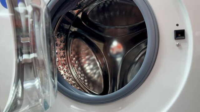 Stainless drum close-up showing door lock and gasket reflections in bright showroom lighting, polished perforated steel tub visible