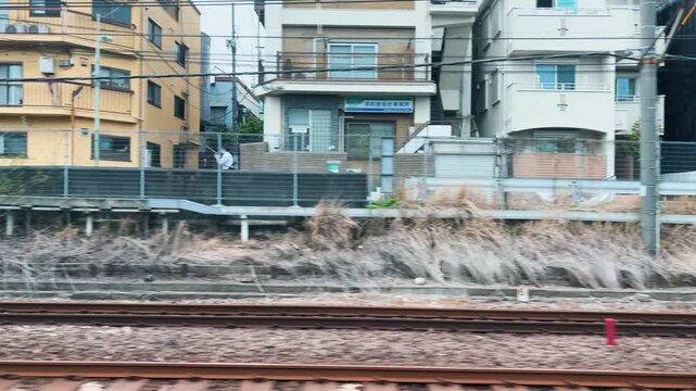 A train passes by typical Japanese residential buildings along the Tokyu Oimachi Line in Setagaya Tokyo. Dense urban houses and electricity cables stand close to the narrow railway tracks.