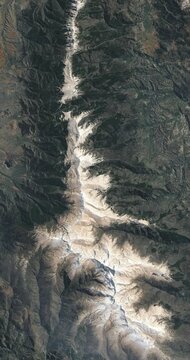 Bird's eye view on mountain ridge covered with snow. Camera is zooming in, rotating counterclockwise. Vertical video. Animation based on image by NASA