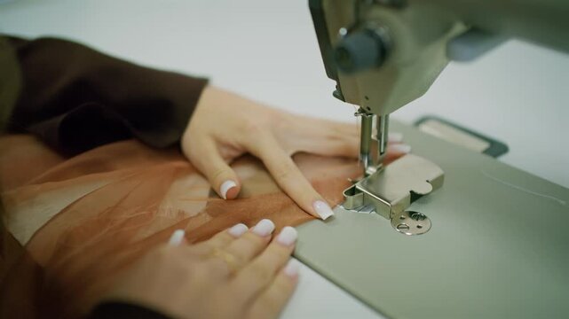 Close up of a person guiding brown sheer fabric under the needle of an industrial sewing machine
