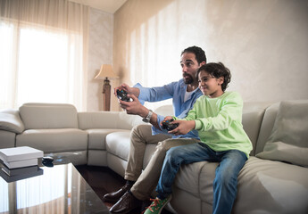Obraz premium Modern Middle Eastern father and son playing video games together in bright living room