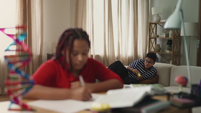 Lazy boy loudly playing video games while his sister tries to do homework