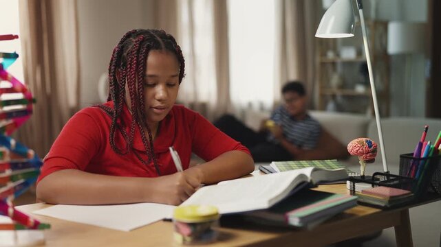 African American girl studying while her lazy older brother plays video games