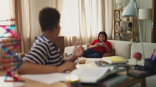 Boy reprimanding sister for loud video gaming while he tries to do homework