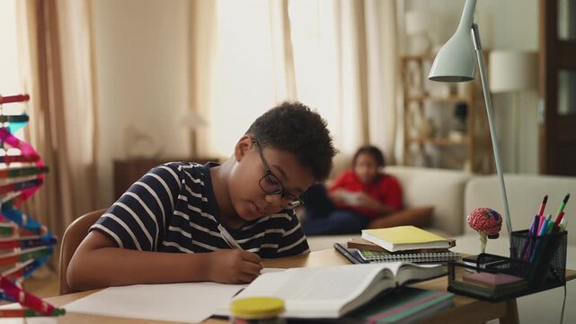 Diligent African American boy studying while lazy sister plays video games