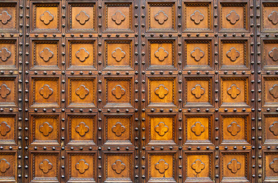 Symmetrical background of a dark wood door featuring carved square panels with quatrefoil rosettes and metal studs