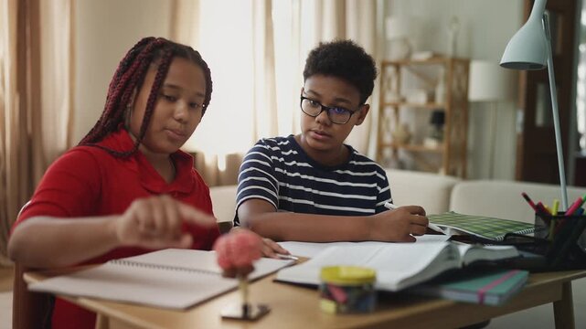 African American siblings doing homework together, writing in notebooks at home