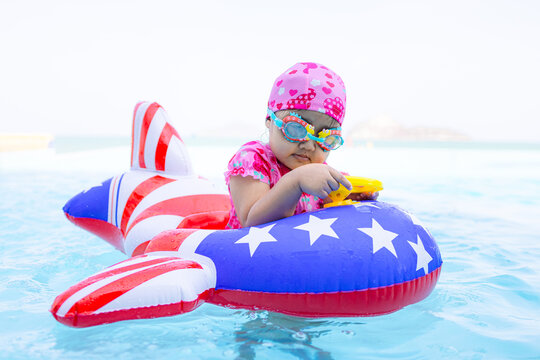 Cute Asian toddler girl playing with airplane inflatable float in luxury swimming pool next to the beach, summer vacation concept,A lovely little Asian child wearing a pink swim cap and goggles,
