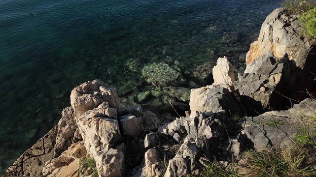Rocky Adriatic Sea coastline with crystal clear turquoise water near Malinska - Krk Island, Croatia. Looking down view from the Paradise Coastal Trail or seaside promenade on a sunny autumn day.