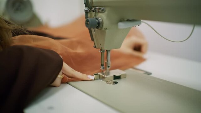 Close up of a person guiding brown sheer fabric under the needle of an industrial sewing machine