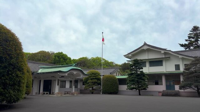 The Japanese flag waves on a flagpole outside the Meiji Jingu shrine office building in Tokyo. This Shinto sanctuary administration complex features two-story white structures.