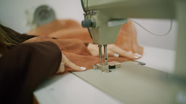 Close up of a person guiding brown sheer fabric under the needle of an industrial sewing machine