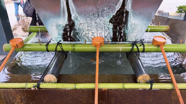 Traditional Japanese temizuya ritual purification fountain at a shinto shrine in Fukuoka. Bamboo pipes water flows into a stone basin with wooden ladles.