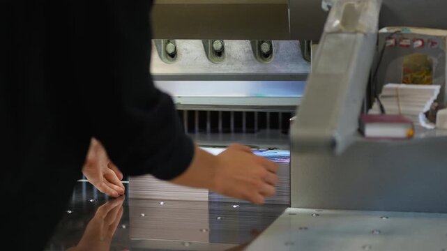Worker cutting paper stack with guillotine machine