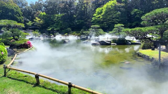 The artificial fog spreads beautifully over the large traditional pond in Ohori Park Japanese Garden in Fukuoka. A dense white mist covers the water surface creating scenic unkai sea of clouds effect