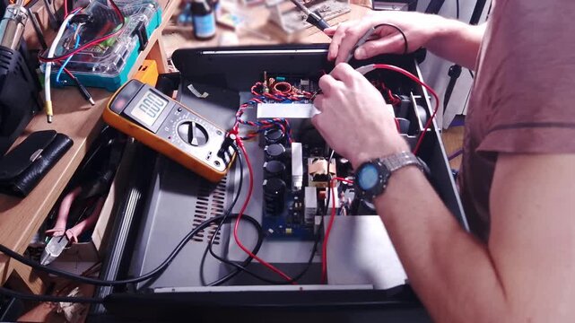 A technician probes electronic components inside a power amplifier using a digital multimeter on a workshop bench. Concept of electronics repair, hardware maintenance, and engineering.