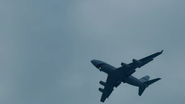 Large four-engine airplane flying high in cloudy overcast sky close up. Silhouette of commercial passenger jet or cargo aircraft takeoff in foggy weather, aviation and air travel background.