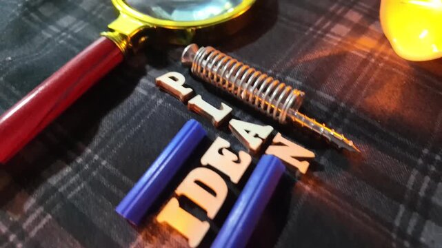 A magnifying glass rests on wooden letters spelling 'PLAN' on a dark patterned background.
