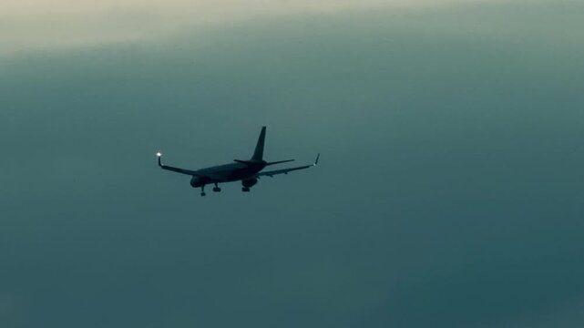 Commercial passenger airplane landing with gear down in cloudy overcast sky. Silhouette of twin-engine jet airliner flight in foggy weather, aviation transport and tourism travel background.