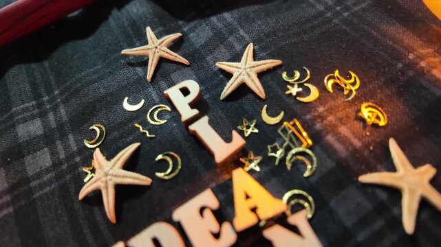 Wooden letters spelling 'IDEA' and 'PLAN' are scattered with starfish and celestial ornaments.