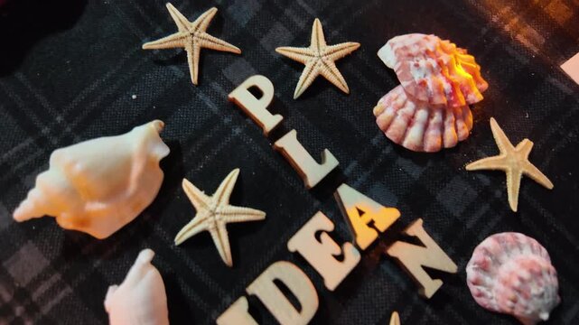 Seashells and starfish surround wooden letters spelling 'IDEA' and 'PLAN' on a dark background.