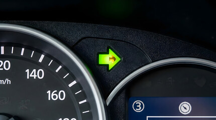 Close-up of car dashboard turn signal indicator light glowing green
