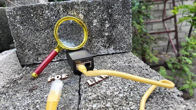 A magnifying glass hovers over network cables and a PoE injector on a textured surface.