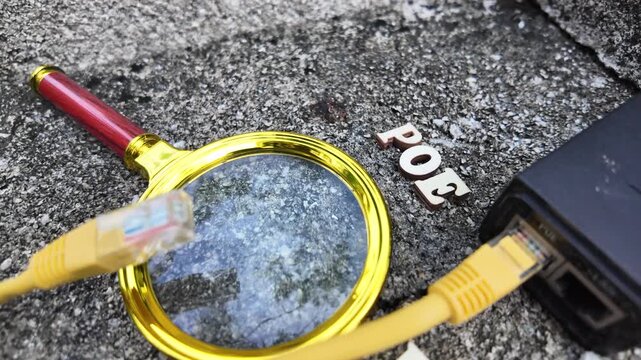 Close-up view of network cables and a PoE injector with a magnifying glass on a rough surface.