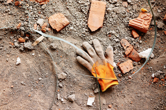 A single dirty orange and grey protective work glove lies abandoned on a dusty concrete floor surrounded by broken red bricks and plastic strapping at a construction site.