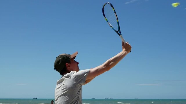Man performing speed badminton serve on sandy beach , summer outdoor training, shuttlecock practice, active lifestyle, fitness.