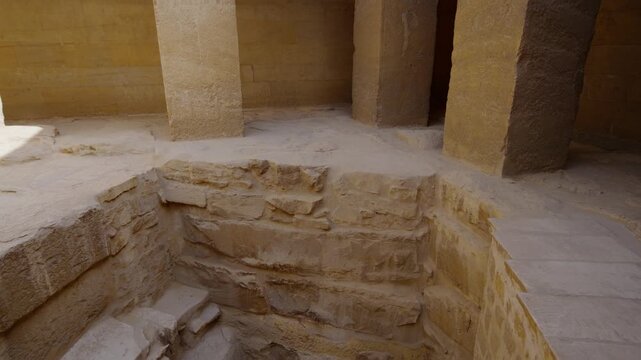 Courtyard of ancient Egyptian mastaba of Ti at Saqqara necropolis, Egypt, with recessed niches, plain limestone walls, dramatic sunlight and shadows on sandy stone floor.