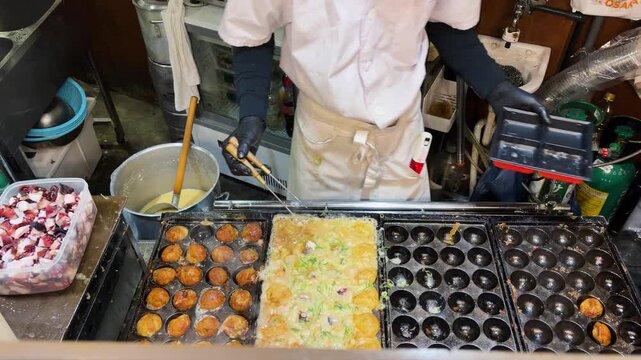 Street food vendor cooking traditional Japanese takoyaki octopus balls in Osaka. Golden batter gets carefully flipped inside a special cast iron grill plate. Freshly diced octopus pieces.