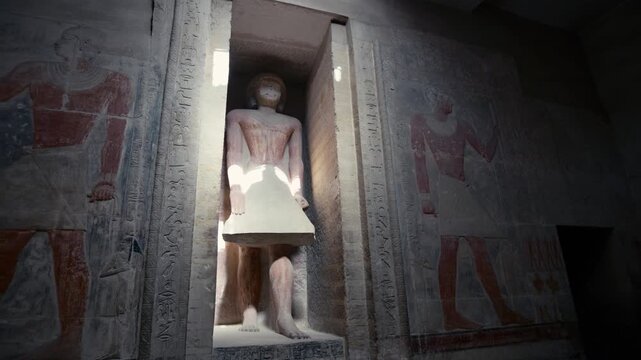 Dramatic sunlit niche with standing limestone figure of Mereruka inside his mastaba tomb at Saqqara, Egypt, flanked by colorful painted relief figures on ancient stone walls.