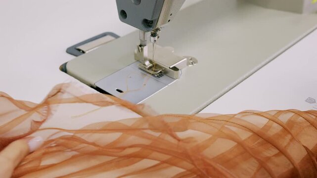 Close up of a designer's hands cutting mustard sewing thread with small red thread snips beside an industrial sewing machine