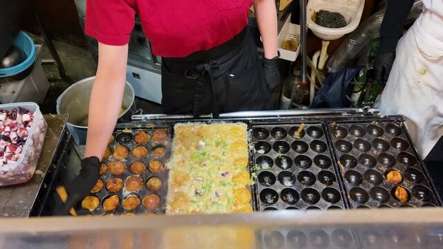 Street food vendor cooking traditional Japanese takoyaki octopus balls in Osaka. Golden batter gets carefully flipped inside a special cast iron grill plate.