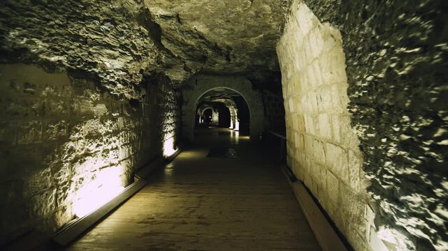 Dark underground corridor with stone arches leading to massive granite sarcophagus inside Serapeum of Saqqara, Egypt, dramatic warm lighting on ancient rock-cut tunnel walls.