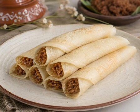 Traditional Bengali Patishapta rice crepes filled with sweet coconut and jaggery stuffing served on rustic ceramic plate authentic winter pitha dessert delicacy 