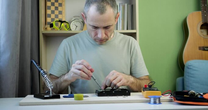Technician repairing electronic device on workbench using screwdriver and precision tools. Small business repair service concept, electronics maintenance and professional troubleshooting in workshop.