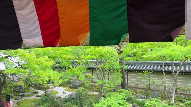 Traditional multicolored goshikimaku banners hang under the eaves of Eikan-do Temple in Kyoto. The historic Japanese Buddhist temple is surrounded by fresh green spring trees. 