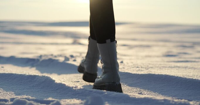 Person walking in snow-covered landscape. Cozy winter atmosphere surrounds individual in warm boots. Bright sunlight illuminates serene snowy environment. Enjoying tranquility of winter day.