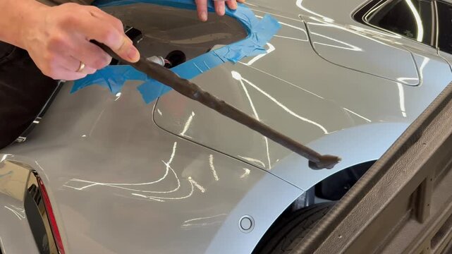 PDR. Process of paintless dent repair on car body. The mechanic at the auto shop with tools to repair dents in car body. Body repair. A specialist repairs a dent on the car body without painting. PDR.
