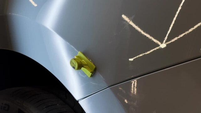 Yellow sticker with glue to make dent removal procedure at car after hail. Process of paintless dent repair on car body. The mechanic at the auto shop with tools to repair dents in car body. PDR. 