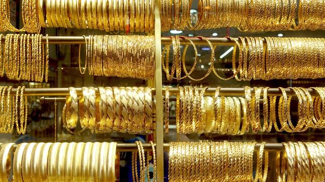 Rows of ornate gold bangles and bracelets shimmer on display rods in a jewelry shop window as the camera slowly reveals a wider selection