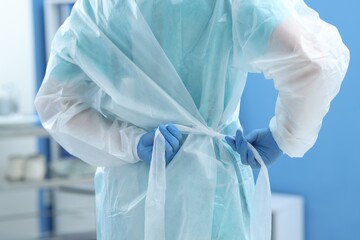 Fototapeta premium Medical worker tying disposable isolation gown indoors, closeup