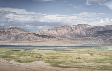 Landscape in the Tien Shan mountains in the Pamirs, mountains in the background and pastures with green fields in a valley with lakes and streams, a summer landscape for the background © Denis