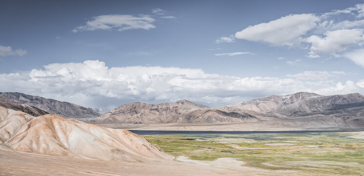 Landscape in the Tien Shan mountains in the Pamirs, mountains in the background and pastures with green fields in a valley with lakes and streams, a summer landscape for the background