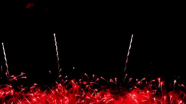 Vibrant fireworks burst upward in a vertical frame, sending bright red, gold, and green trails across a dark night sky, capturing dynamic motion and festive energy during a celebration.